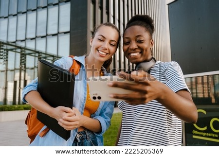 Young multiracial women smiling and taking selfie photo on cellphone at city street