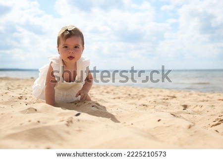 A portrait of a 1 year old caucasian baby girl on the sandy beach on a sunny warm day at Baltic Sea