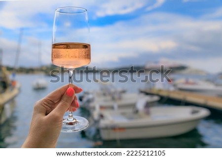 Woman holding a glass of rose wine with Mediterranean Sea and boats in background in Villefranche sur Mer Old Town on French Riviera, South of France Royalty-Free Stock Photo #2225212105