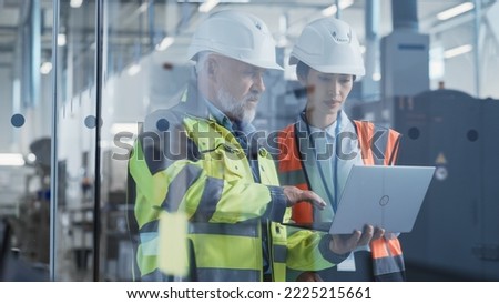 Two Professional Heavy Industry Engineers Wearing Safety Uniform and Hard Hats Discussing Industrial Machine Part on Laptop Computer. Asian Specialist and Middle Aged Technician at Work. Royalty-Free Stock Photo #2225215661