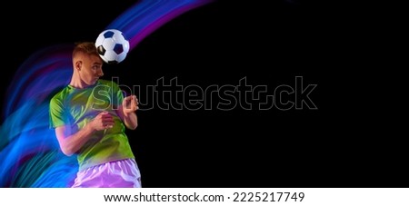 Studio shot of professional football player playing soccer isolated on dark background neon light filter. Sport, fashion, championship, challenges. Athlete jumping, kick the ball