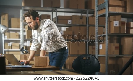 Inventory Manager Preparing a Small Cardboard Parcel for Postage. Stylish Young Male Small Business Owner Working on Laptop Computer in Warehouse Facility Royalty-Free Stock Photo #2225224041