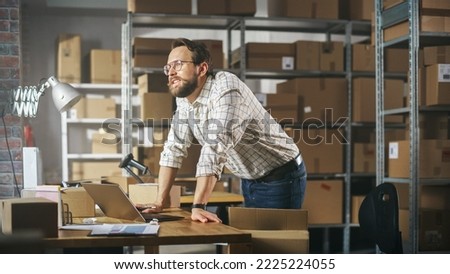 Stylish Small Business Owner Preparing a Small Parcel for Postage. Happy Inventory Manager Thinking About His Successful Career. Working on Laptop Computer in Warehouse Facility.