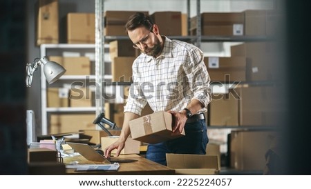 Small Business Owner of a Retail Online Shop Preparing a Small Cardboard Parcel for Postage. Stylish Young Inventory Manager Working on Laptop Computer in Warehouse Facility. Royalty-Free Stock Photo #2225224057