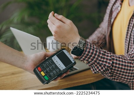 Cropped man he wearing shirt hold wireless bank payment terminal smart watch process credit card payments sit at table in coffee shop cafe rest in free time. Freelance mobile office business concept