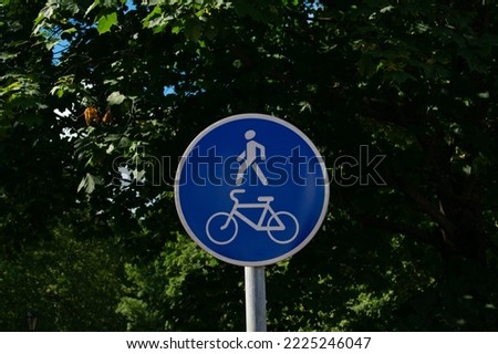 Bicycle and pedestrian lane road sign on pole post, large blue round  against the background of green trees