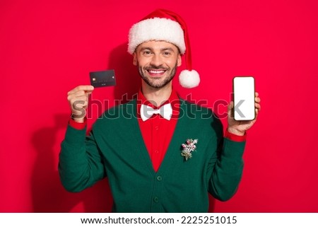 Photo of funny sweet guy dressed xmas green cardigan bowtie rising bank card modern gadget empty space isolated red color background