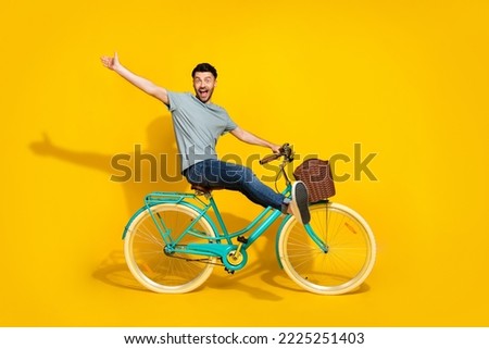 Side profile photo of funky crazy excited man wear gray t-shirt denim jeans sitting new retro bicycle raise palm hello friends isolated on yellow color background Royalty-Free Stock Photo #2225251403