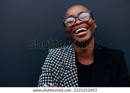A business portrait of a smiling black woman outdoors standing in front of a black wall.