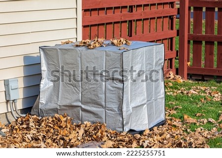 House air conditioning unit with protective cover during fall season. Concept of home air conditioning, hvac, repair, service, winterize and maintenance. Royalty-Free Stock Photo #2225255751