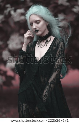 Dark goth girl standing in the forest, portrait of a wiccan witch performing magic Royalty-Free Stock Photo #2225267671