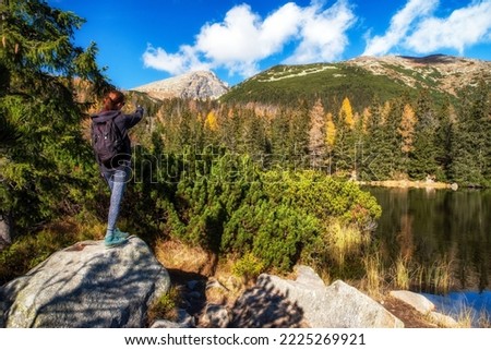 Girl hiker on the rock showing on  peak Krivan in High Tatras mountains in Slovakia. Lake Jamske pleso at background