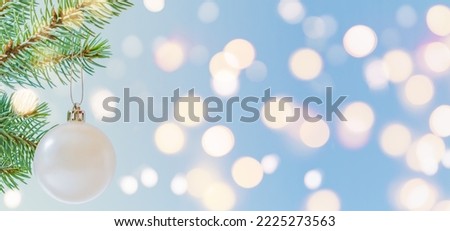 White Christmas ball on a fir tree branch with festive bokeh on a blue background.  Wide horizontal banner with copy space. Winter and christmas concept