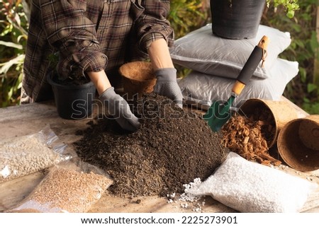 Gardening concept. A young woman mixes potting soil, prepares the soil for planting vegetables and herbs in the house, mixes potting soil, perlite, vermiculite, peat, worm, coconut flakes, rice husk.  Royalty-Free Stock Photo #2225273901