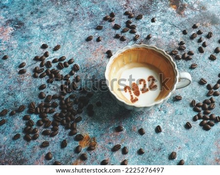 Goodbye 2022, holidays food art theme coffee cup with number 2022 over frothy surface at bottom of cup on rustic blue background with coffee beans. (top view, selective focus, space for text)