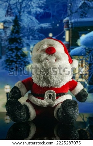Santa claus doll with snowy village background and christmas decorations at night