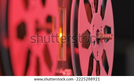 Reel to reel tape recorder on black background with red light. Vintage music player with round metallic bobbins close up. Retro magnetic tape reel. Popular disco trends 70s, 80s. Royalty-Free Stock Photo #2225288921