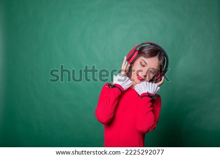 pretty cheerful girl listening different song rock dancing isolated on green color background.Positive smiling young woman with red headphones in red dress while listening music. She enjoying song