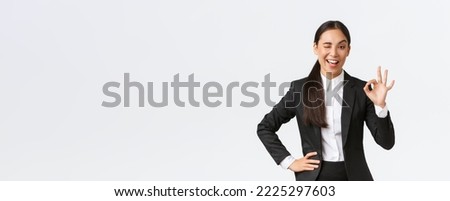 Assertive and confident young asian businesswoman got all under control, wink and show okay gesture to encourage deal is done, good job, nice work or approval gesture, standing pleased.