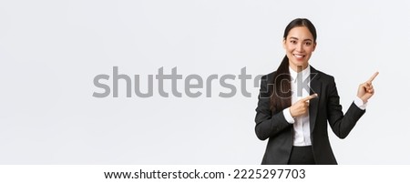 Confident asian female entrepreneur, saleswoman in suit introduce product, showing place to clients. Businesswoman smiling and pointing fingers right at banner, standing white background.