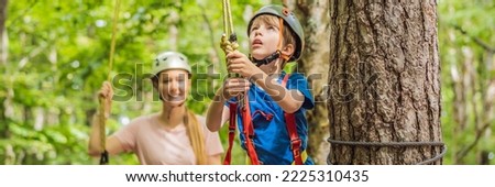 BANNER, LONG FORMAT Mother and son climbing in extreme road trolley zipline in forest on carabiner safety link on tree to tree top rope adventure park. Family weekend children kids activities concept Royalty-Free Stock Photo #2225310435