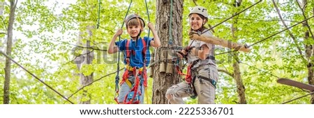 BANNER, LONG FORMAT Mother and son climbing in extreme road trolley zipline in forest on carabiner safety link on tree to tree top rope adventure park. Family weekend children kids activities concept Royalty-Free Stock Photo #2225336701