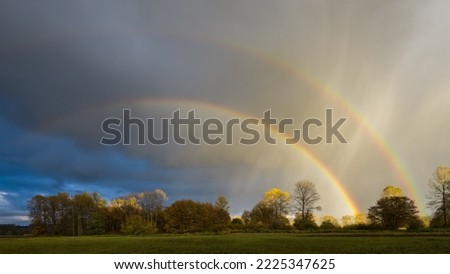 Double rainbow passing through rain shafts above rural countryside in fall