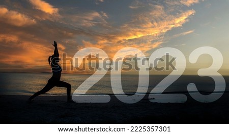 Happy new year card 2023. Silhouette of A girl doing Yoga warrior I pose on tropical beach with sunset sky background, practicing yoga on the beach