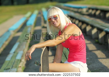 athletic girl with skateboard on the background of the old benches of the stadium