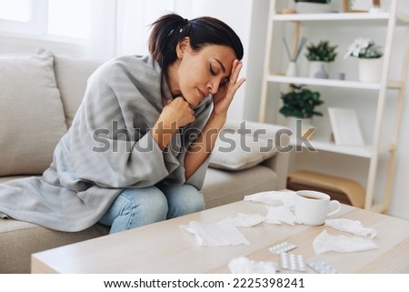 A woman with a cold pills is treated at home chooses which medicines to take and self-medicates, checks the expiration date while sitting at home on the couch, temperature, allergies and covid-19 Royalty-Free Stock Photo #2225398241