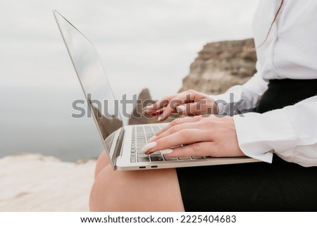 Silhouette of laptop and cup on the beach over sea sunset. Sparkling sea water on background. Freelancer, blogger working on notebook on the beach.