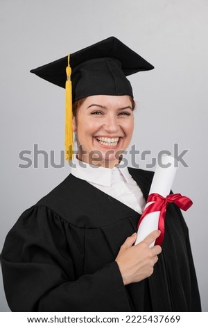 Smiling woman in graduation gown holding diploma on white background. Vertical photo.