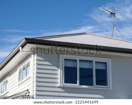 Residential detached house with white wooden plank walls and metal roof. Eaves and gutter with downspout. Royalty-Free Stock Photo #2225441699