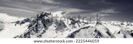 Black and white panorama of high snow-capped mountain peaks and beautiful sky with clouds at sun windy day. Caucasus Mountains in winter, region Dombay, mount Dombay-Ulgen. Royalty-Free Stock Photo #2225446059