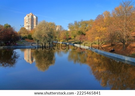 The photo was taken in a public park in the city of Odessa. The picture shows a lake reflecting trees with autumn foliage and a blue sky.