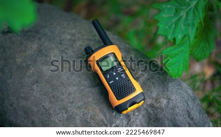 An orange-colored walkie-talkie on a granite stone in the forest. The intercom of rescuers. A means for radio communication in the campaign.