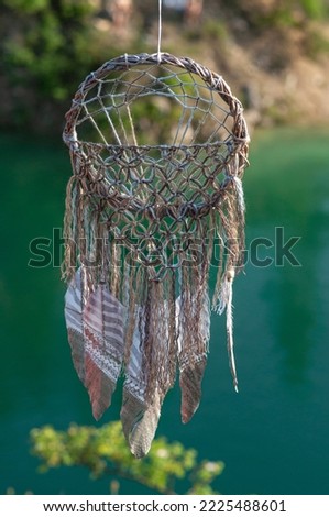 Handmade dreamcatcher close up tribal bohemian craft hanging over the azure lake outdoors 