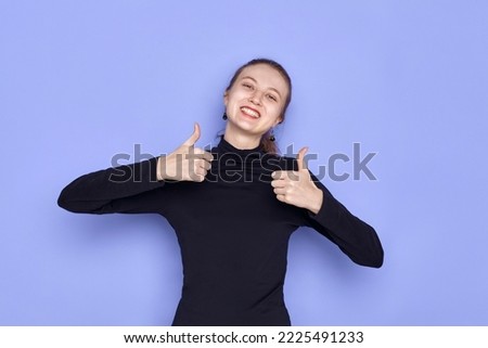 a happy woman smiles broadly standing on a purple background and gives a thumbs up