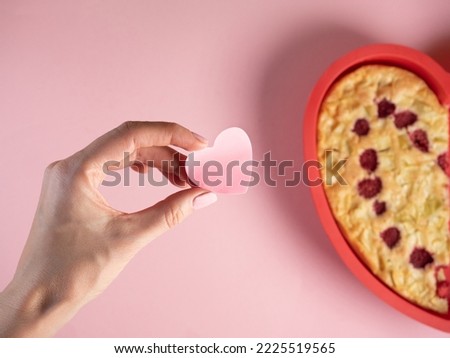 Woman hand hold heart shape pink paper, heart shape half apple pie on pink background. Celebrating Valentine's Day  Royalty-Free Stock Photo #2225519565