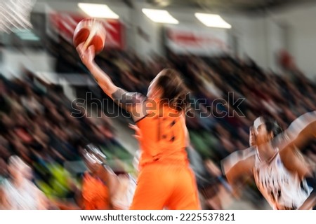 Woman player throws the ball into the basket during basketball match. Intentional blured picture (tattoo on the arm was additionally smudged)