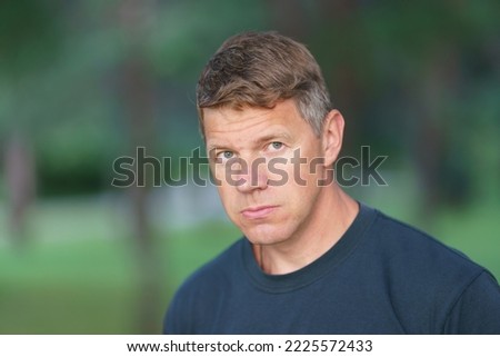 Handsome male model in the parkland in the sunny summer day. He has short blond hair. He is so sad. Man is upset about something. Green natural background. Close up great image Royalty-Free Stock Photo #2225572433