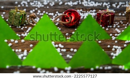 Green paper trees on rustic wooden background covered with little white balls and and red Christmas jingle bell and gifts