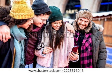 Group of millenial trendy friends walking at city center using mobile phone - Tech life style concept with happy young people on winter fashion clothes having fun day together - Bright vivid filter