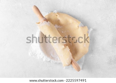 Raw crust pie dough into a baking dish with a rolling pin on a light gray background. Top view of homemade pie crust on the table. Home baking concept, pie crust recipe, hobby home bakery, top view