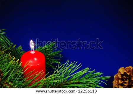 Burning candle near a pine branch with cone on blue background