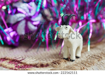 Plasticine world - little homemade white goat with black horns and hooves on purple background, selective focus and place for text