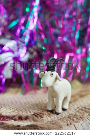 Plasticine world - little homemade white goat with black horns and hooves on purple background, selective focus and place for text