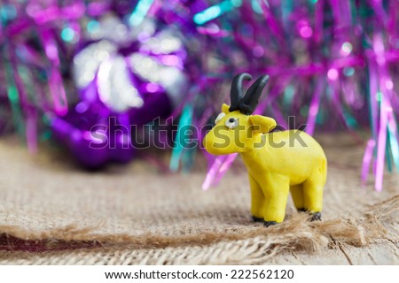 Plasticine world - little homemade yellow goat with black horns and hooves stand on a wooden floor, selective focus and place for text
