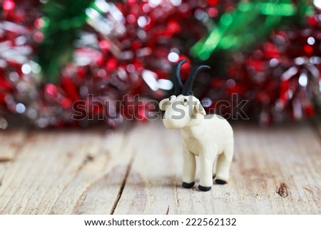 Plasticine world - little homemade white goat with black horns and hooves stand on a wooden floor, selective focus and place for text 