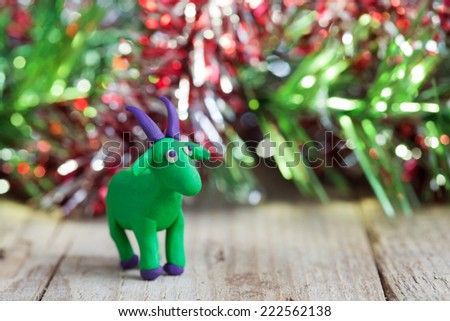 Plasticine world - little homemade green goat with purple horns and hooves stand on a wooden floor, selective focus and place for text